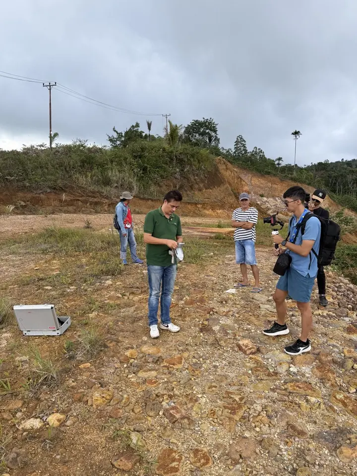 Sebuah tim di lokasi tambang di lereng bukit, sementara seorang mengukur dengan peralatan.